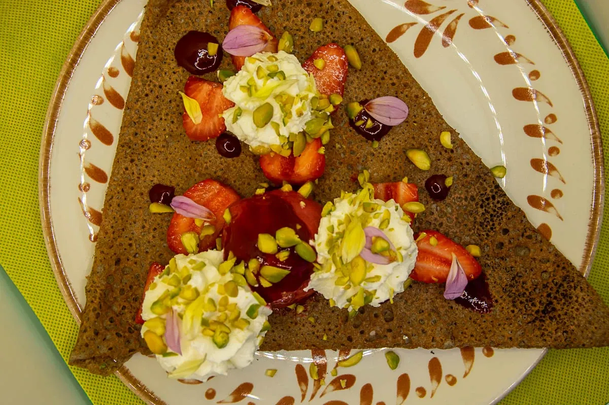 Galette sucrée aux fraises, chantilly et pistaches, sur une assiette à motifs